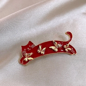 Macro shot of a red enamel cat brooch with gold butterfly motifs on champagne satin fabric