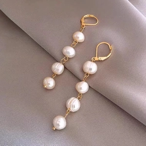 Elegant gold earrings with white baroque freshwater pearls on grey silk fabric backdrop