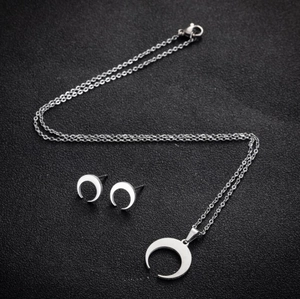 Silver crescent moon necklace and stud earrings set on a black textured background