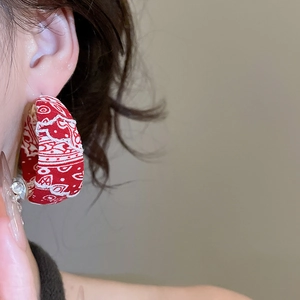 Détail de grandes créoles en C avec tissu imprimé paisley rouge portées par un mannequin