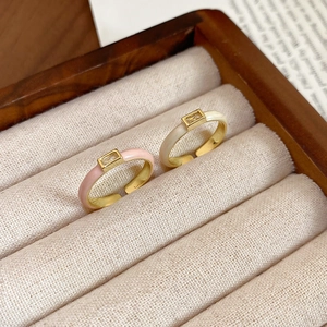 Detail of square zircon rings in pink and cream enamel with adjustable gold bands