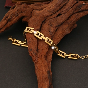 Macro view of golden H-link chain bracelet on dark wood base with luxury lighting