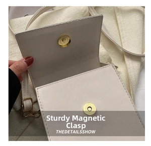 Detailed macro view of the gold magnetic closure on a cream-white textured crossbody bag