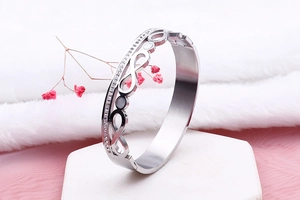 Detail of silver infinity bangle featuring double row zircons on a white geometric stand