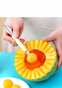 Close-up of dual-head stainless steel fruit baller carving a melon ball in a kitchen