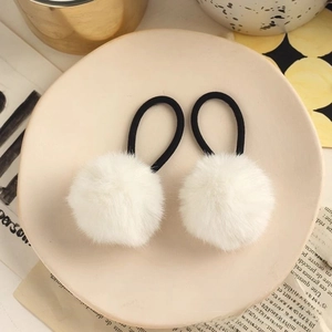 Close-up of white plush pompom hair ties on a ceramic plate with warm home decor