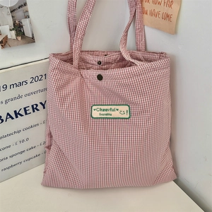 Close-up of red plaid tote bag featuring metal snap closure and Cheerful graphic patch