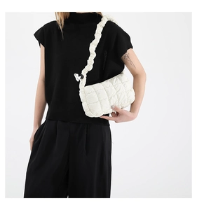 Close-up of a white quilted crossbody bag featuring a unique ruched handle design