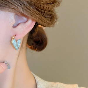 Close-up of heart-shaped blue earrings with red dots worn on a model's ear