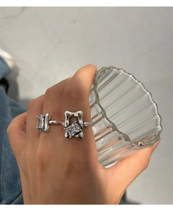 Detail of two silver 925 rings with square zircons worn by a hand holding a glass