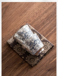 Detalle de tazas de té plateadas con relieve de dragón azul sobre un tapete vintage