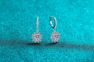 Macro shot of silver sunflower moissanite earrings with sparkling clear zircon on green background