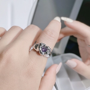 Detailed close-up of a silver ring with a sparkling heart-shaped purple gemstone on a finger