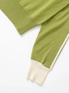 Detailed close-up of grass green knit sweater with cream ribbed cuff and fine texture