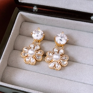Dettaglio macro di orecchini a fiore con perle placcati oro 18K e zirconi su velluto grigio