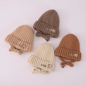 Detail of four knit baby earflap hats in neutral tones with Lucky bear embroidery