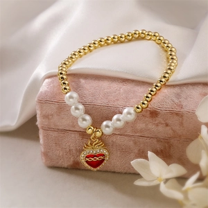 Detailed shot of golden bead bracelet with red enamel heart and zircon pendant