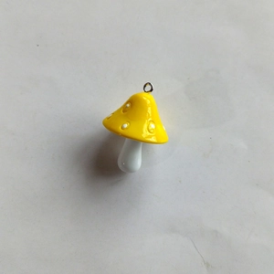 Detailed view of a yellow resin mushroom charm with white spots and a small metal loop