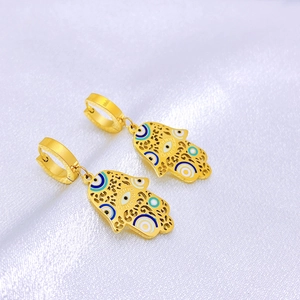 Golden Hamsa Hand earrings with blue Evil Eye enamel details on white silk background