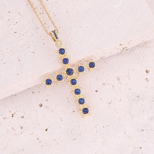 18K gold plated cross pendant necklace with blue cubic zirconia on stone background