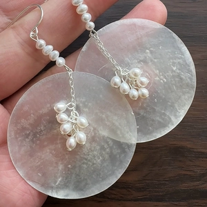 Elegant pearl and shell disc drop earrings with silver hooks on dark wood background