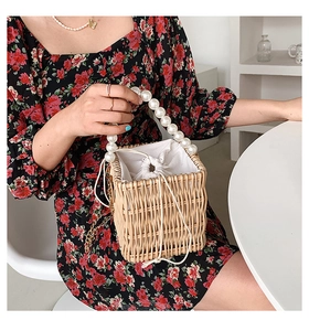 Detail of woven straw bag featuring large pearl handle and golden chain strap