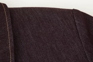 Détail des coutures contrastées et de la texture en sergé sur l'épaule d'une veste marron
