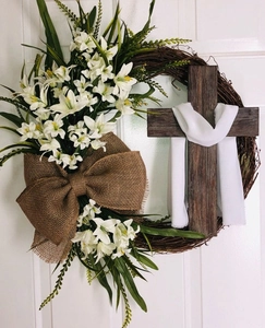 Detail of Easter cross wreath with white lilies and burlap bow on a wooden door