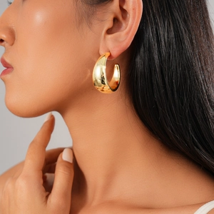 Close-up of chunky gold-tone C-shaped hoop earrings with a polished metallic finish