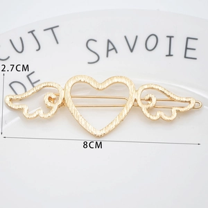 Golden heart wing hair clip with brushed metal texture shown in a white ceramic dish