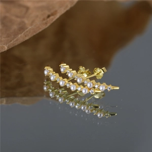 Detail of gold curve earrings with pearls and crystal rhinestones on dark surface