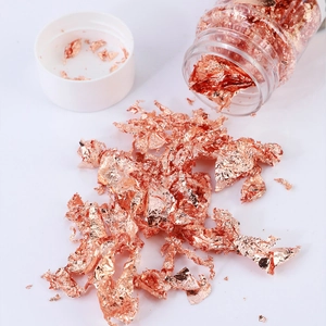 Close-up of rose gold foil flakes spilling from a plastic jar for DIY art and crafts