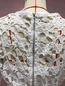 Close-up of the elegant white floral lace pattern and the metal zipper closure on the back