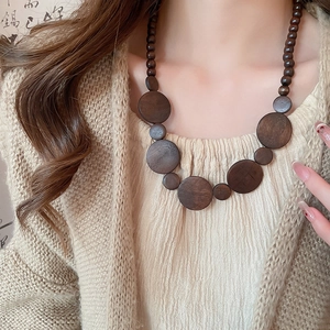 Close-up of vintage wooden bead necklace with geometric round pendants on model wearing beige