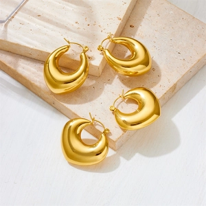 Close-up of golden hollow heart and oval earrings on a textured stone surface