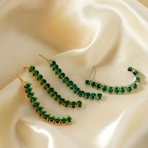 Detail view of curved fringe stud earrings with emerald green zircons on satin