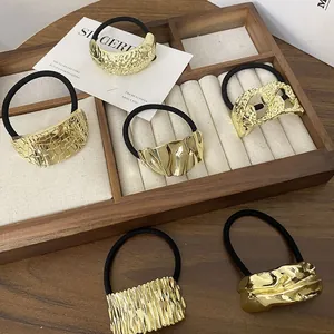 Detailed view of six gold alloy ponytail holders with unique geometric textures on a tray