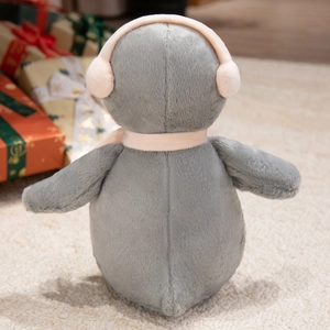 Rear view of a plush penguin toy wearing pink earmuffs and scarf on a cozy carpet