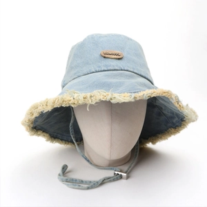 Close-up of light blue denim bucket hat with frayed edges and metal logo detail