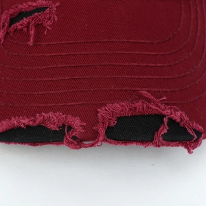 Macro detail of wine red distressed cotton baseball cap with raw edge frayed design