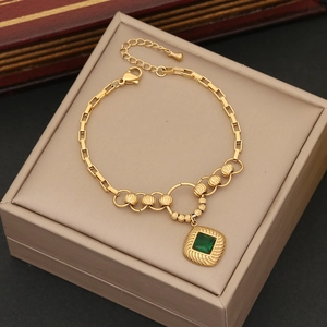 Golden chain bracelet featuring a green square gemstone pendant on a jewelry case