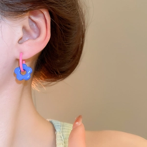 Close-up of vibrant blue flower earrings with pink hooks on model, dopamine style