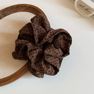 Close-up of leopard print fabric scrunchie on a wooden tray with elegant pearl accents