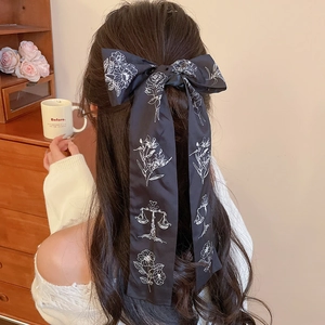 Detail of a black fabric bow hair tie with white floral print on a satin ribbon