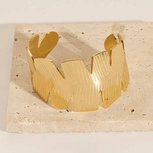 Detailed view of golden C-shaped stainless steel cuff with embossed leaf texture