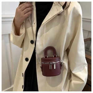 Détail du sac cylindre en cuir bordeaux avec chaîne argentée porté sur un trench-coat