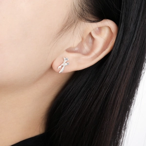 Irregular branch-shaped silver earrings with small diamonds on a model's ear