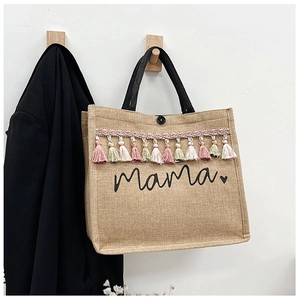 Detailed texture of jute tote bag with 'Mama' print and colorful bohemian tassels