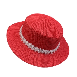 Close-up of red straw hat featuring elegant white lace and pearl beaded ribbon detail
