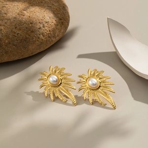 Detail of gold palm tree earrings with white pearl inlay on a natural stone background